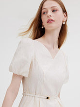 A lady with pearl earrings wears a white dress.